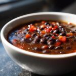 Close-up of a bowl filled with delicious Zesty Black Bean Soup, garnished with red peppers.