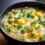 Close-up of a bowl of Egg Drop Soup with visible egg yolks and green onions, a classic comfort food.