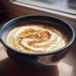 A bowl of creamy Roasted Cauliflower Soup, garnished with cream and spices.