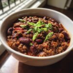 Close-up of a bowl of delicious venison chili, garnished with fresh green onions.