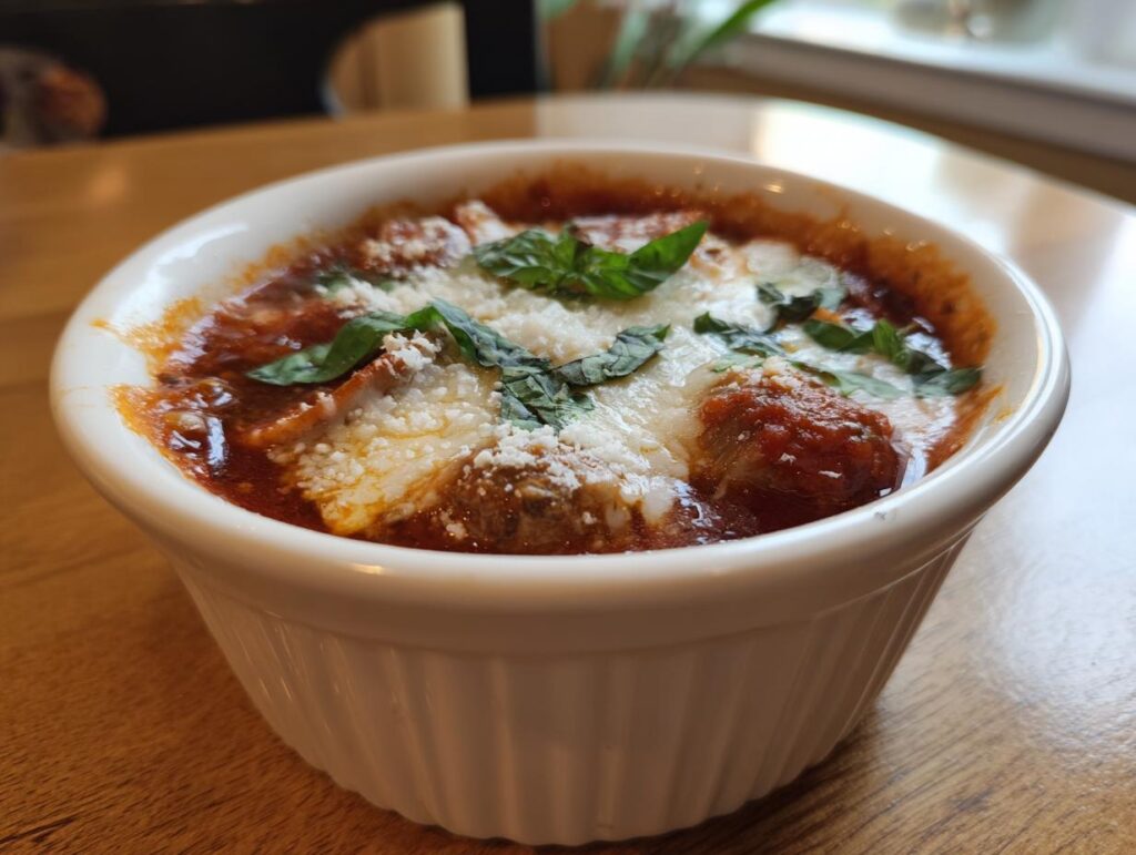 Close-up of a bowl of Pizza Soup with meatballs, cheese, and basil.