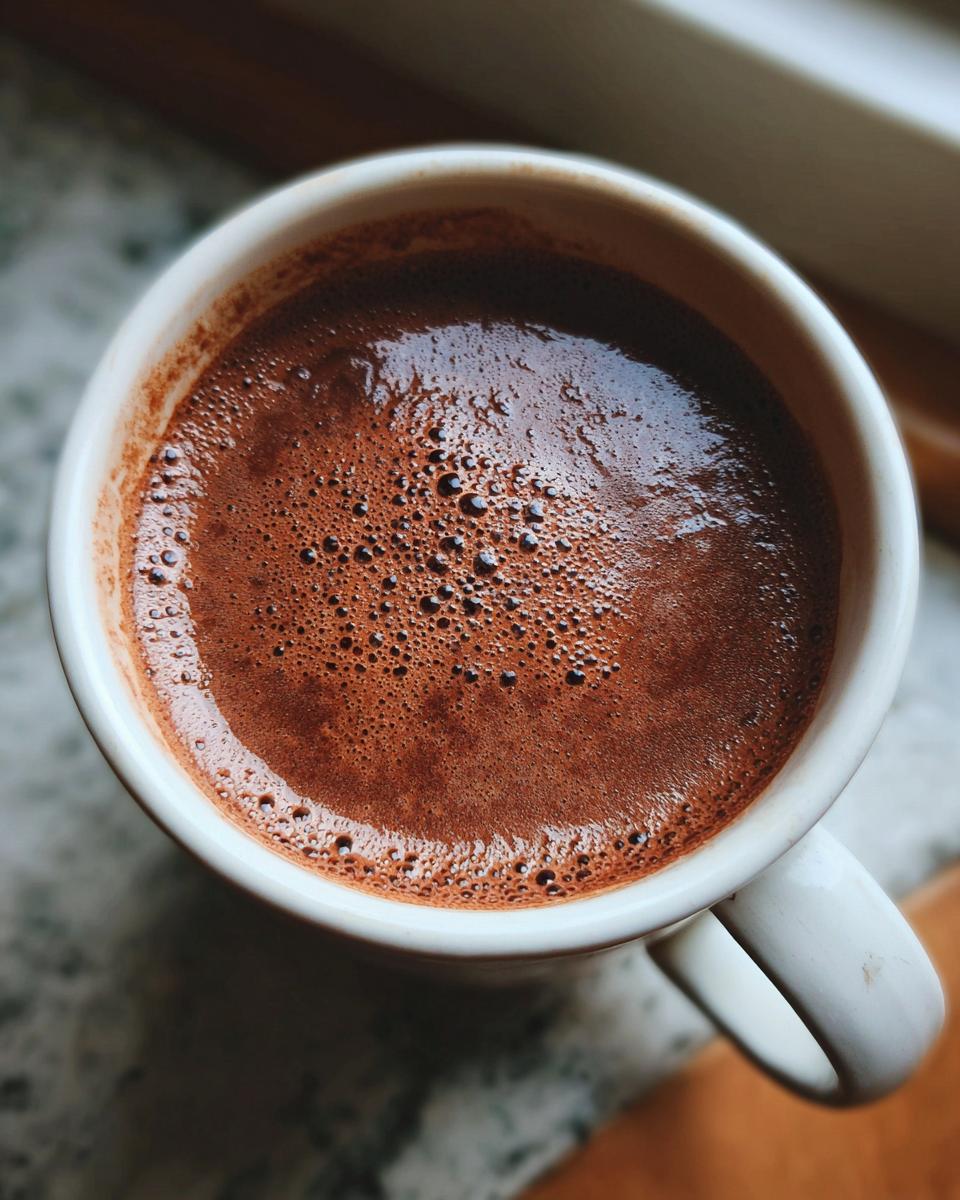 Overhead shot of a mug filled with The Creamiest Chocolate Recipe, with bubbles on top.
