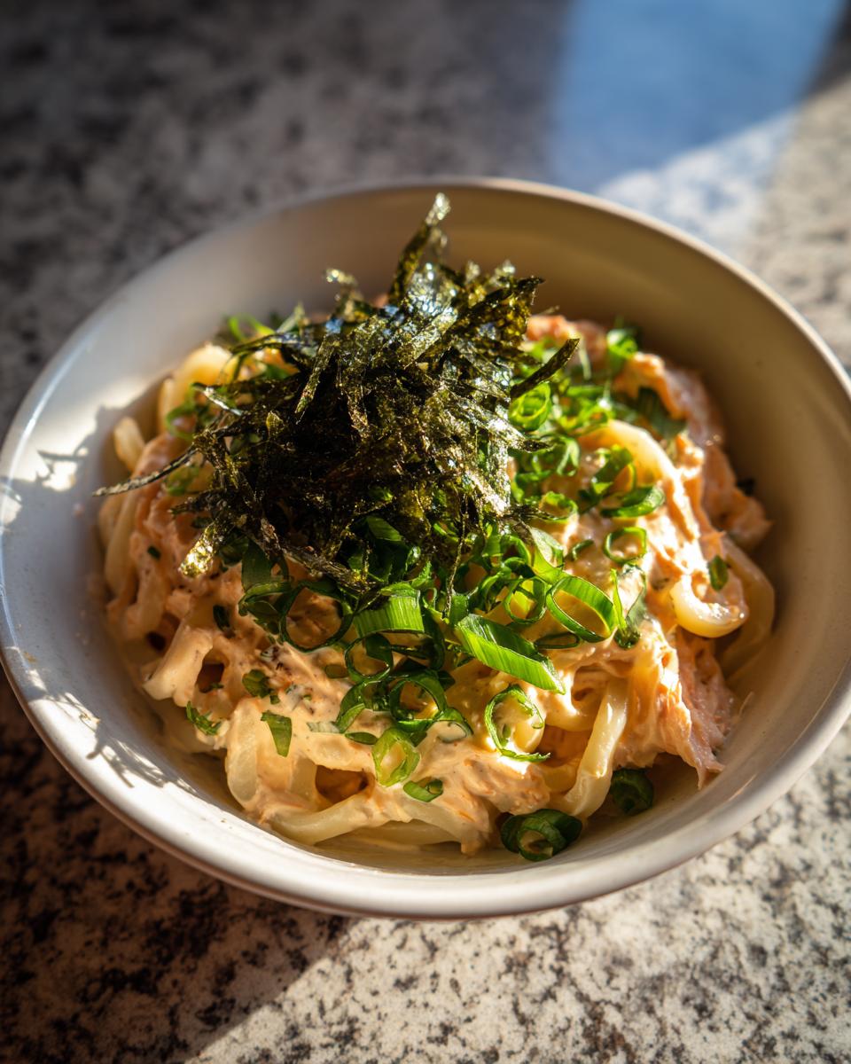 Close-up of a bowl of Creamy Mentaiko Udon, topped with seaweed and green onions.