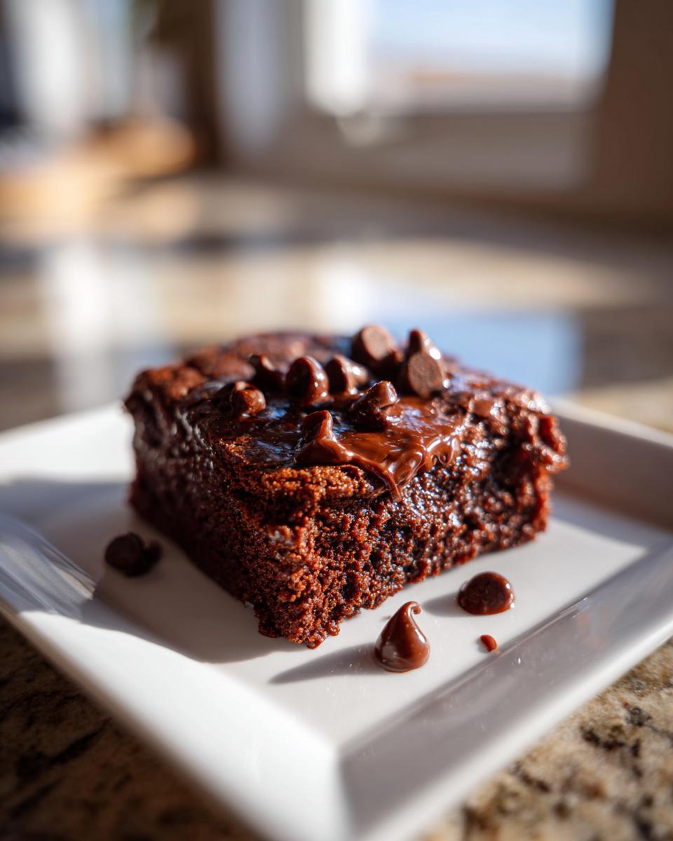 A square slice of brownie, topped with chocolate chips and sauce, This Dessert Feels Illegal It’s So Good.