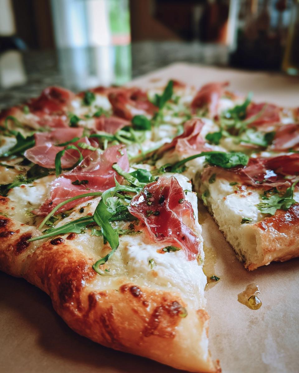 Amazing Prosciutto Pea Shoot Pizza in 35 Min 5 Close-up of a Prosciutto and Pea Shoot Pizza with a slice removed, showing the ingredients.