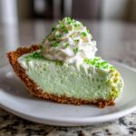 A slice of No Bake Shamrock Shake Pie on a white plate, topped with whipped cream and sprinkles.