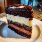 Close-up of a slice of Triple Chocolate Mousse Cake on a white plate, showing layers of mousse and cake.