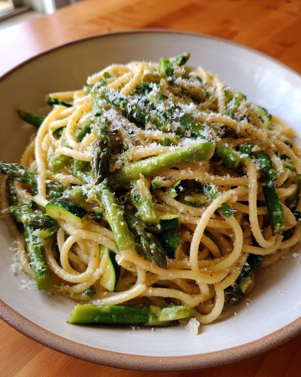 A bowl of delicious asparagus and zucchini pasta salad, garnished with cheese.