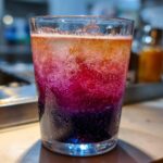 Close-up of a layered beach cocktail in a glass, with vibrant colors and bubbles.