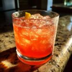 Close-up of a vibrant cocktail with ice and a lemon peel garnish; perfect for 12 Big-Batch Cocktails.