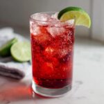 A vibrant red Driveway Drink in a glass with ice and a lime wedge.