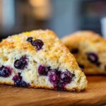 Close-up of a delicious Lemon Blueberry Scone on a wooden board, with fresh blueberries.
