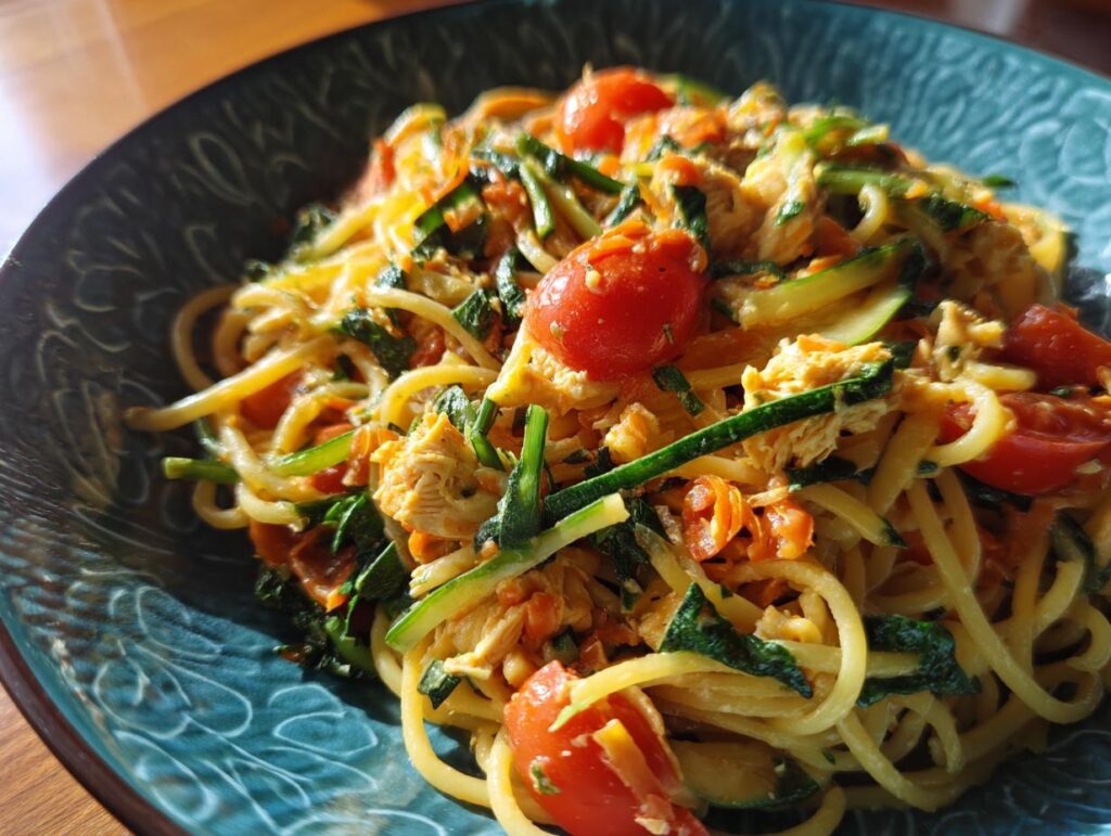 Close-up of pasta salad and chicken with tomatoes and zucchini in a blue bowl.