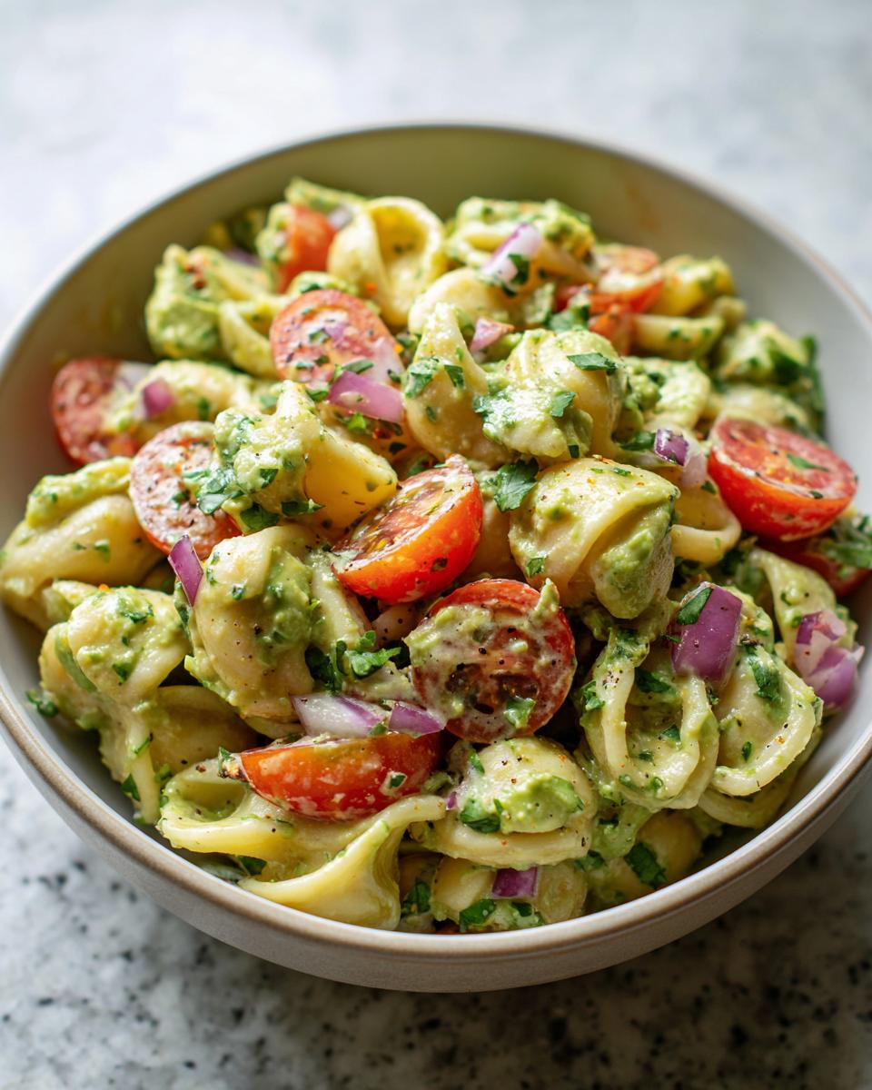 Close-up of a bowl of pasta salad avocado with cherry tomatoes and red onion.