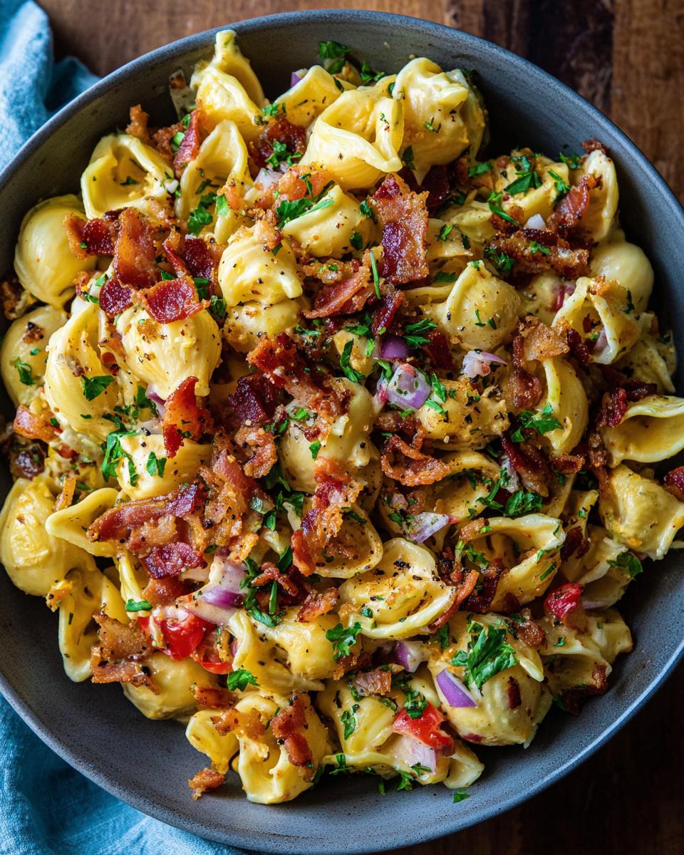 Overhead shot of a bowl filled with pasta salad bacon, garnished with parsley and red onion.