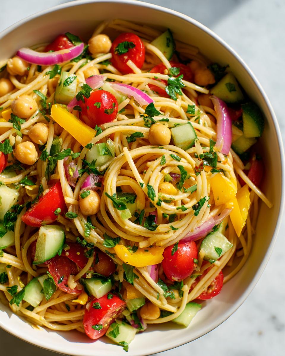 Overhead shot of a pasta salad chickpeas bowl with tomatoes, cucumbers, and red onion.
