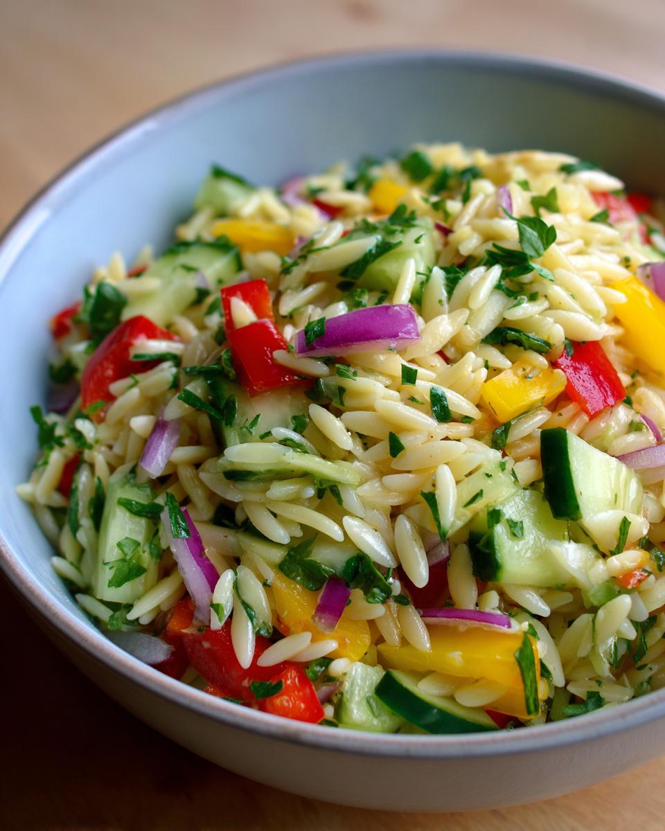 Close-up of a pasta salad orzo with colorful vegetables in a bowl. Includes red onion, bell peppers, and cucumber.