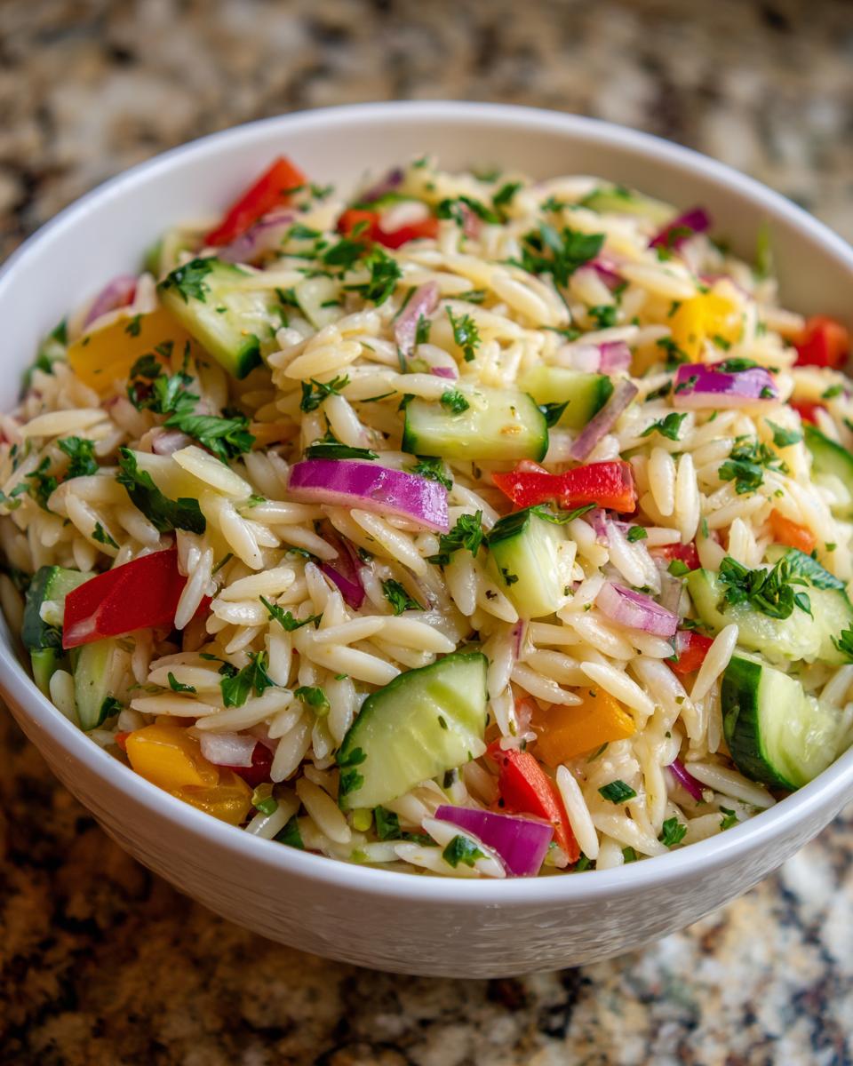 Close-up of pasta salad orzo with cucumbers, red onion, peppers, and parsley.