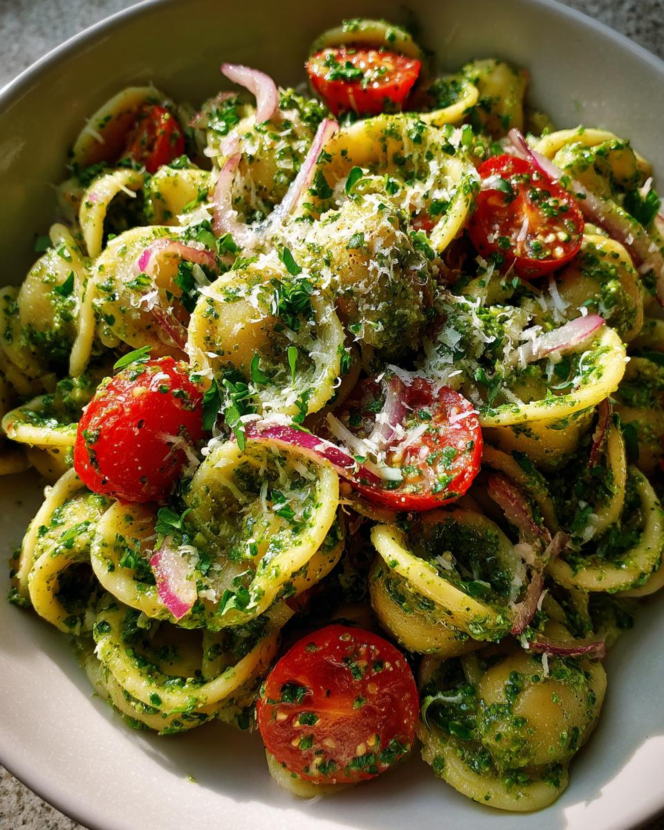 Close-up of pasta salad pesto with cherry tomatoes, red onion, and parmesan cheese.