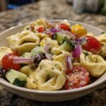 Close-up of a bowl of pasta salad tortellini with tomatoes, cucumbers, and olives.