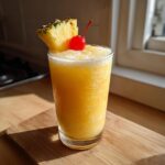 A refreshing Perfect Piña Colada cocktail in a glass, garnished with pineapple and a cherry.
