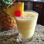 A Perfect Piña Colada cocktail in a glass, garnished with pineapple and a cherry.