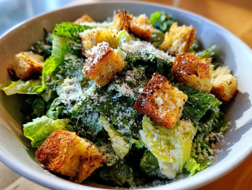 Close-up of a bowl of Spring Greens Caesar with homemade croutons and parmesan cheese.