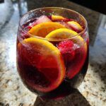 Close-up of a glass of refreshing Summer Sangria with orange slices, lemon, and raspberries.