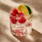Close-up of a summer vodka cocktail with raspberries, lime, and ice.