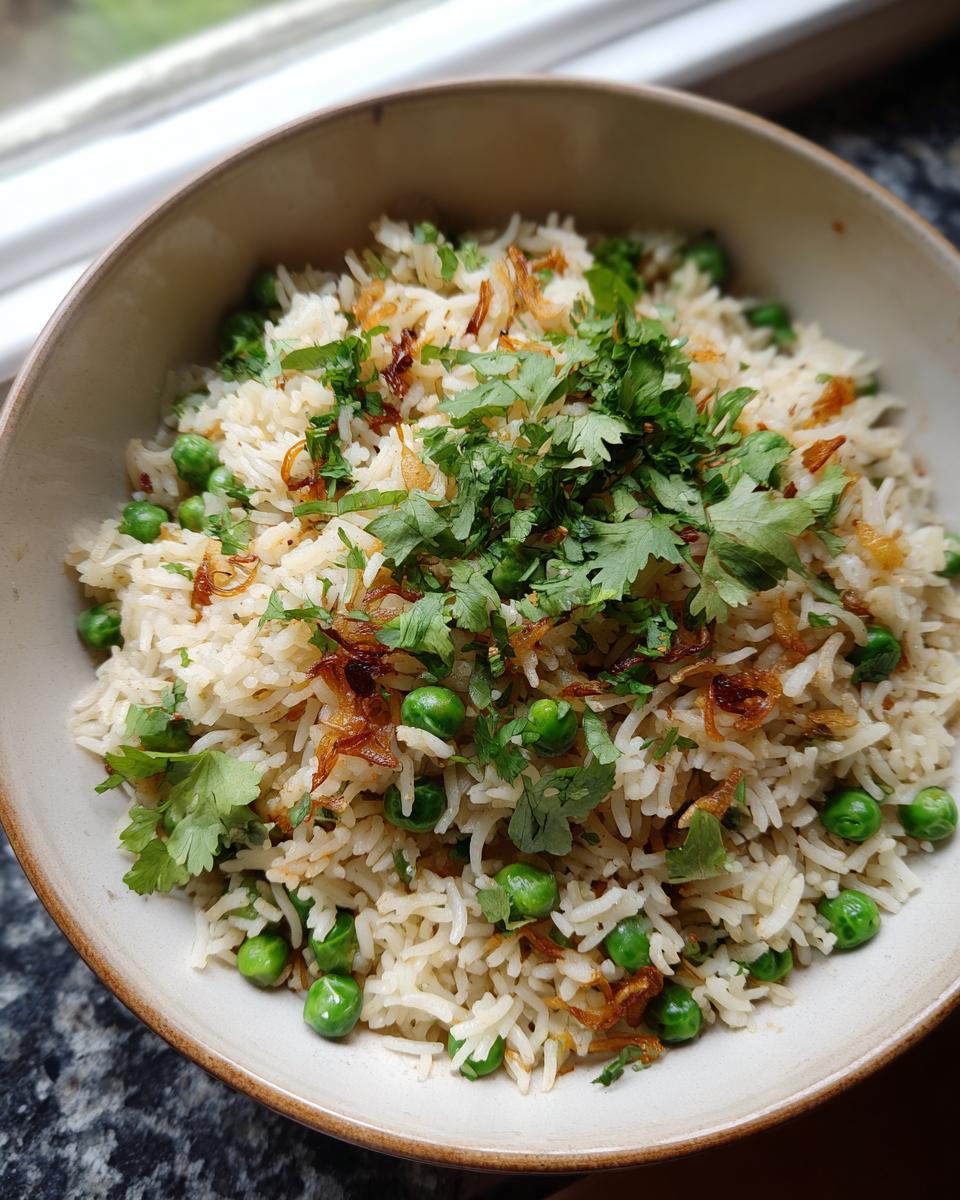 Overhead shot of a bowl of Sweet Pea & Shallot Pulao, garnished with fresh herbs and fried onions.